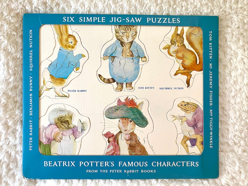 May include: A vintage jigsaw puzzle featuring six characters from Beatrix Potter's books, including Peter Rabbit and Tom Kitten. The puzzle pieces are shaped like the characters and are set against a light background with a blue border. The text "SIX SIMPLE JIG-SAW PUZZLES" is visible.