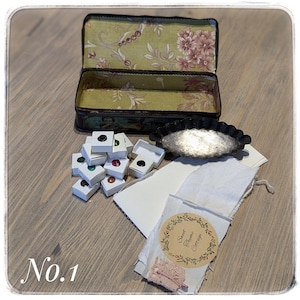May include: A vintage tin box with a floral pattern, open to reveal a set of small paint pans, a white fabric square with a label that reads "Sweet Thyme Cottage", and a small metal baking dish.