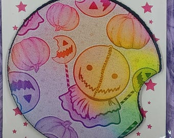 May include: Two car coasters with a Halloween theme. The coasters feature a colorful design with jack-o'-lanterns and a character with a stitched mouth. The text "CAR COASTERS" is at the top. The coasters are packaged in clear plastic.