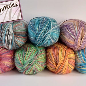 Könnte beinhalten: Eine Sammlung von acht bunten Garnknäuel mit verschiedenen Streifen und Mustern. Das Garn ist in Pyramidenform angeordnet. Das Garn ist mit "Memories" beschriftet.