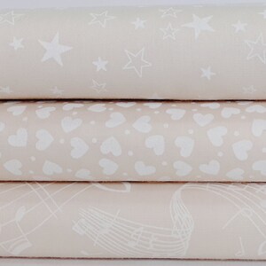 Könnte beinhalten: Drei Stoffstücke mit verschiedenen Mustern. Das obere Stück ist ein hellbeiger Stoff mit einem weißen Sternmuster. Das mittlere Stück ist ein hellbeiger Stoff mit einem weißen Herzmuster. Das untere Stück ist ein hellbeiger Stoff mit einem weißen Notenmuster.