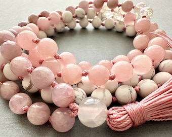 May include: A pink and white gemstone mala necklace with a pink tassel. The necklace is made with rose quartz and white howlite beads.