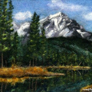 May include: A needle felted artwork depicting a mountain range with snow-capped peaks, a lake reflecting the mountains, and a foreground of evergreen trees.
