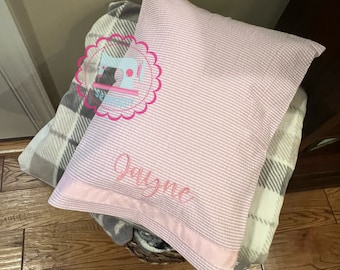 May include: A pink and white striped pillow with a pink satin trim and the name "Jayne" embroidered on it.