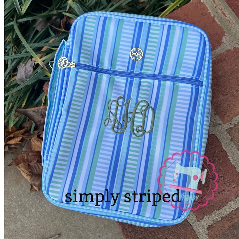 Puede incluir: Una bolsa de almuerzo a rayas azules y blancas con cierre de cremallera y herrajes dorados. La bolsa presenta un monograma y el texto "simply striped". La bolsa est&aacute; dise&ntilde;ada con rayas verticales en tonos azules y verdes.