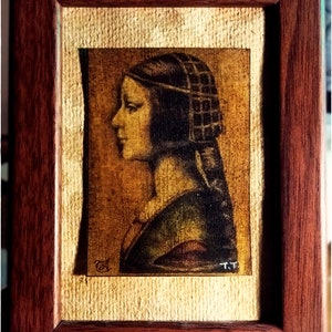 May include: A framed artwork featuring a profile portrait of a person with a dark head covering. The artwork is in a dark wooden frame with a textured, light-colored background. The artist's initials "T.T." are visible.
