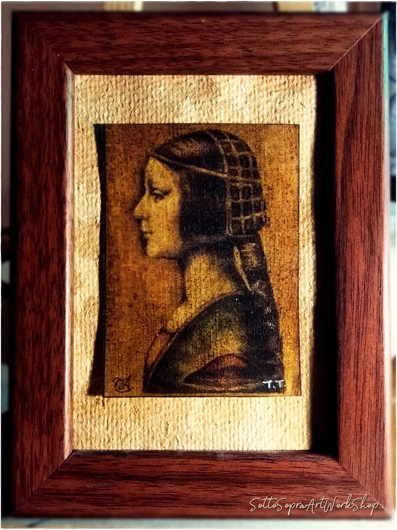 May include: A framed artwork featuring a profile portrait of a person with a dark head covering. The artwork is in a dark wooden frame with a textured, light-colored background. The artist's initials "T.T." are visible.