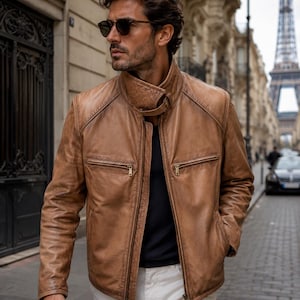 May include: A brown leather jacket with a zip-up front, two chest pockets, and a stand-up collar. The jacket is worn over a black shirt and paired with white pants. The background features a European street scene with the Eiffel Tower.