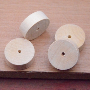 Puede incluir: Cuatro círculos de madera sin terminar con un agujero en el centro. Los círculos están dispuestos en semicírculo sobre una superficie de madera marrón claro.