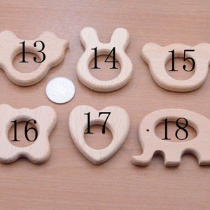 May include: A collection of six wooden baby teethers in various shapes: a butterfly, bunny, bear, flower, heart, and elephant. Each teether has a smooth, natural wood finish and a central hole for easy gripping. A coin is included for size reference.