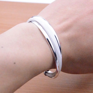 Peut inclure: Un bracelet jonc en argent avec un motif tissé. Le bracelet est ouvert et a une finition lisse et polie.