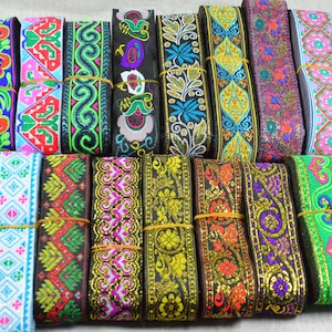 Könnte beinhalten: Eine Sammlung farbenfroher, bestickter Bänder mit verschiedenen floralen und geometrischen Mustern. Die Bänder weisen eine Reihe von Farben auf, darunter Blau, Grün, Rot und Gold. Jedes Band ist etwa 2,5 cm breit.