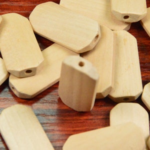 May include: A pile of unfinished, natural wood, rectangular-shaped tags with rounded edges and a hole in the centre.