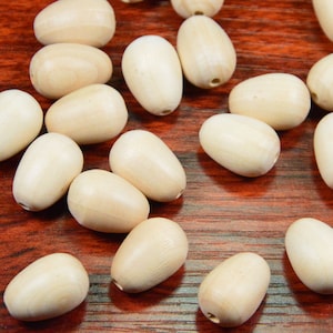 Puede incluir: Una colección de cuentas de madera natural de color beige claro. Las cuentas son de forma ovalada y tienen un acabado liso y pulido.