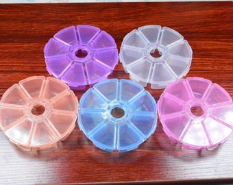 May include: Five round plastic containers with lids, each divided into eight sections. The containers are clear, purple, pink, light blue, and orange.