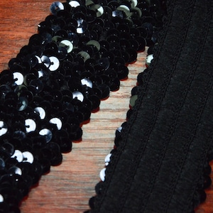 May include: Black sequined trim and black ribbed elastic trim. Both trims are on a wooden surface.