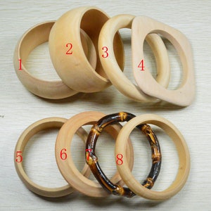 May include: Eight wooden and bamboo bangle bracelets in various shapes and sizes. The bracelets are all natural wood tones.