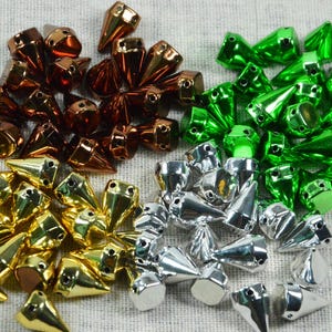 May include: An assortment of metallic cone-shaped beads in gold, silver, bronze, and green. The beads have a pointed tip and a flat base with a hole for stringing. The beads are scattered on a textured, light-colored surface.