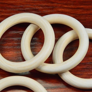 May include: Four unfinished wooden rings, stacked on top of each other, on a dark wood surface.