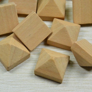 Può includere: Un gruppo di blocchi di legno quadrati e piramidali di colore legno naturale. I blocchi sono sparsi su una superficie marrone chiaro.