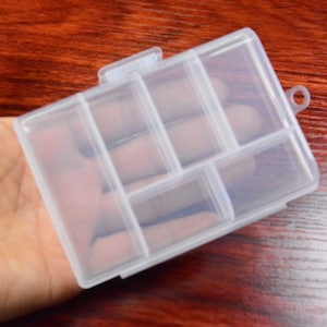 May include: A clear plastic storage box with a hinged lid and a small handle. The box has six compartments.