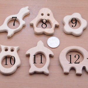 May include: A collection of six wooden baby teethers in various animal shapes, including a bird, penguin, flower, owl, turtle, and elephant. Each teether has a circular opening in the center and is made of light-colored wood.