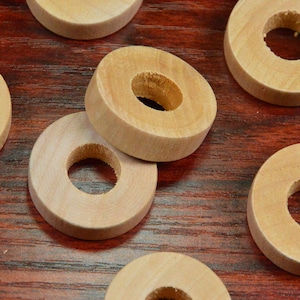 May include: Six wooden rings with a hole in the center. The rings are stacked on top of each other and are on a wooden surface.