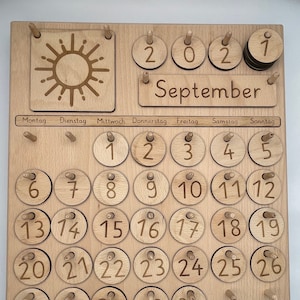 Könnte beinhalten: Ein Holzkalender mit einem Sonnenmotiv und dem Text "2021 September". Der Kalender hat ein Raster mit nummerierten Kreisen für jeden Tag des Monats.