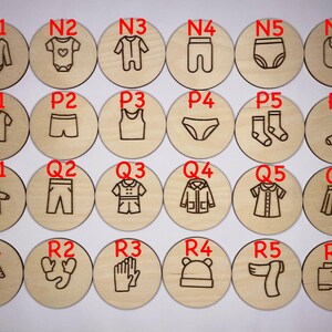 May include: Twenty-four wooden circles with different clothing items and accessories engraved on them. The circles are labeled with letters and numbers, such as N1, P2, Q3, and R4.