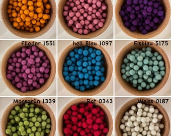 May include: Nine bowls of colorful felt balls in various shades of orange, pink, purple, magenta, blue, green, red, and white. Each bowl has a label with the color name and a number.