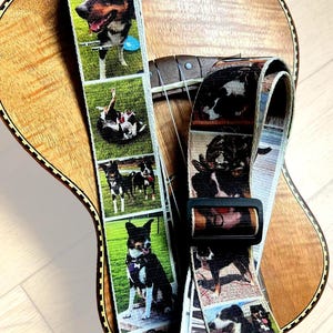 May include: A custom guitar strap featuring a repeating photo collage of a black, white, and tan dog in various outdoor settings. The strap includes a black plastic adjustable buckle and is displayed resting on the wooden body of a stringed instrument.