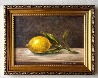 May include: A framed oil painting of a lemon with green leaves. The lemon is yellow and sits on a light brown surface. The painting is in a gold ornate frame. The artist's signature, "Malinovsky", is visible.