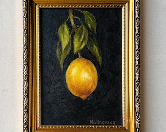 May include: A framed painting of a single yellow lemon hanging from a branch with green leaves against a black background. The artist's signature, "Malinovsky", is visible in the bottom right corner of the painting.