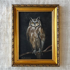 May include: A framed painting of an owl with brown and white feathers, perched on a branch. The painting is set against a dark background and signed "Malinevsky" in the bottom left corner.