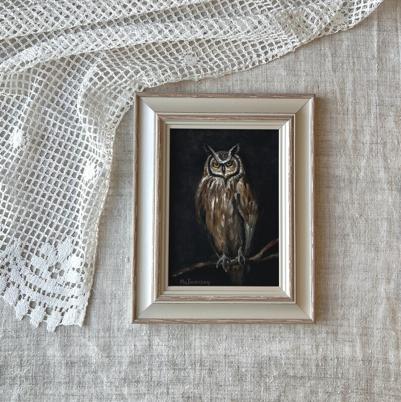 May include: A framed painting of a brown and white owl with yellow eyes, perched on a branch against a dark background. The painting is signed "Malinowsky" in the bottom left corner.