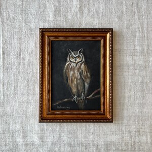 May include: A framed painting of an owl with brown and gray feathers, perched on a branch. The owl has yellow eyes and is looking directly at the viewer. The painting is set against a dark background and is signed "Malinovsky" in the bottom left corner.