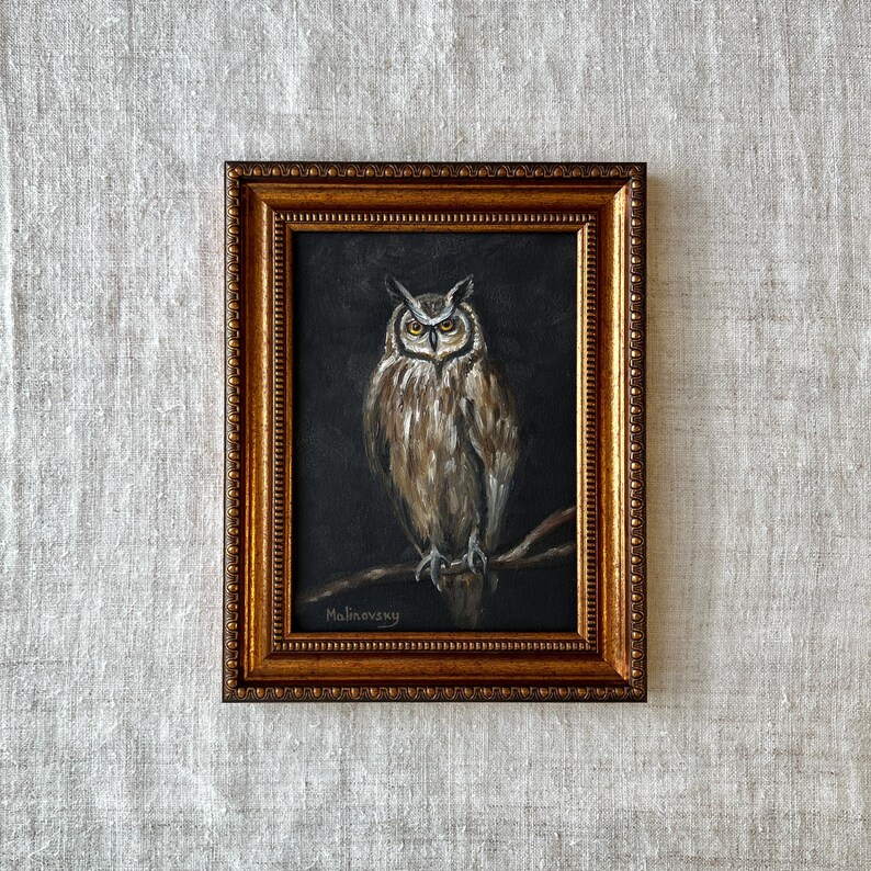 May include: A framed painting of an owl with brown and gray feathers, perched on a branch. The owl has yellow eyes and is looking directly at the viewer. The painting is set against a dark background and is signed "Malinovsky" in the bottom left corner.