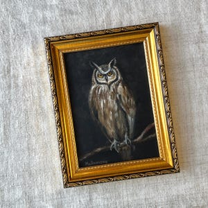 May include: A framed painting of an owl with brown and white feathers, perched on a branch. The owl has yellow eyes and is looking directly at the viewer. The painting is signed "Malinovsky" in the bottom left corner.