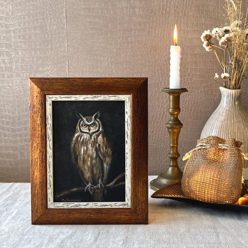 May include: A framed painting of an owl with brown and white feathers, set against a dark background. The frame is a dark wood with a white inner border. The painting is signed "Maliceva" in the bottom left corner.