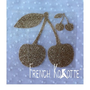 May include: Gold glitter iron-on patch with a design of two cherries with stems and leaves. The text "French Kokotte" is below the cherries.