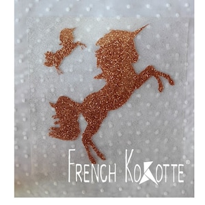 Peut inclure: Une silhouette de licorne en paillettes cuivrées avec une plus petite silhouette de licorne au-dessus. L'image est sur un fond blanc avec de petits points blancs. Le texte "French Kokotte" est en bas de l'image.
