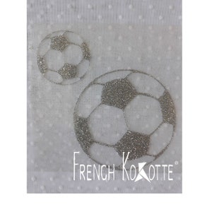 Peut inclure: Deux ballons de football argentés à paillettes sur un fond blanc avec un motif de pois blancs. Le plus grand ballon de football est au premier plan et le plus petit ballon de football est à l'arrière-plan. Le texte "French Kokotte" est imprimé sous les ballons de football.