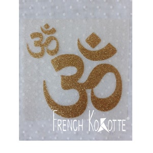 May include: Gold glitter Om symbol on a white background with the text "French Kokotte" below.