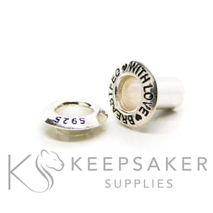 May include: Two silver-coloured metal jewellery findings. One is a small, flat ring with the text "S925" and the other is a cylindrical shape with the text "BREATHE WITH LOVE" and heart symbols. The findings are on a white background.