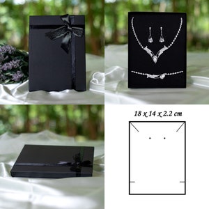 May include: Black jewelry box with a black ribbon and bow. The box is open and shows a silver necklace and earrings set with rhinestones. The box measures 18 x 14 x 2.2 inches.