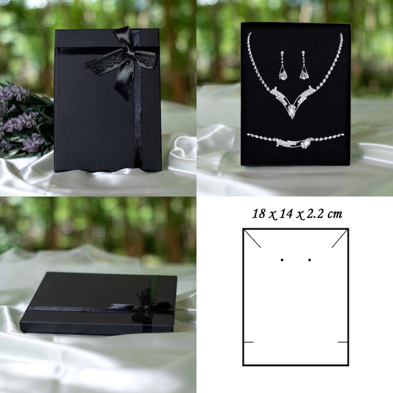 May include: Black jewelry box with a black ribbon and bow. The box is open and shows a silver necklace and earrings set with rhinestones. The box measures 18 x 14 x 2.2 inches.