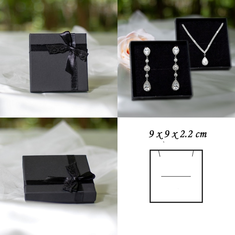 May include: Two black gift boxes with black ribbon bows. One box contains a pair of silver teardrop earrings with clear stones. The other box contains a silver necklace with a teardrop pendant. The boxes are 9 x 9 x 2.2 cm.