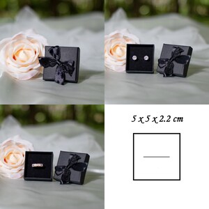 May include: Two black gift boxes with black ribbon bows. One box contains a pair of small silver earrings. The other box contains a silver ring. The boxes are 5 x 5 x 2.2 cm.