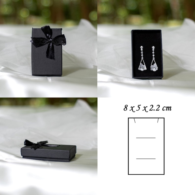 May include: Two black gift boxes with black ribbon bows. One box is 8 x 5 x 2.2 cm and contains a pair of silver dangle earrings with clear stones.