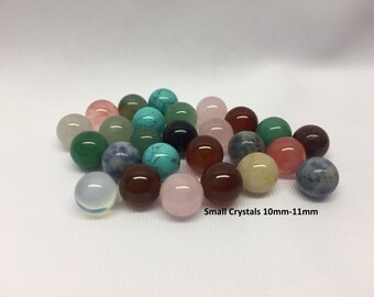 May include: A selection of small, polished crystal spheres in a variety of colours, including green, pink, blue, and brown. The crystals are approximately 10-11mm in diameter. Text on the image reads "Small Crystals 10mm-11mm."